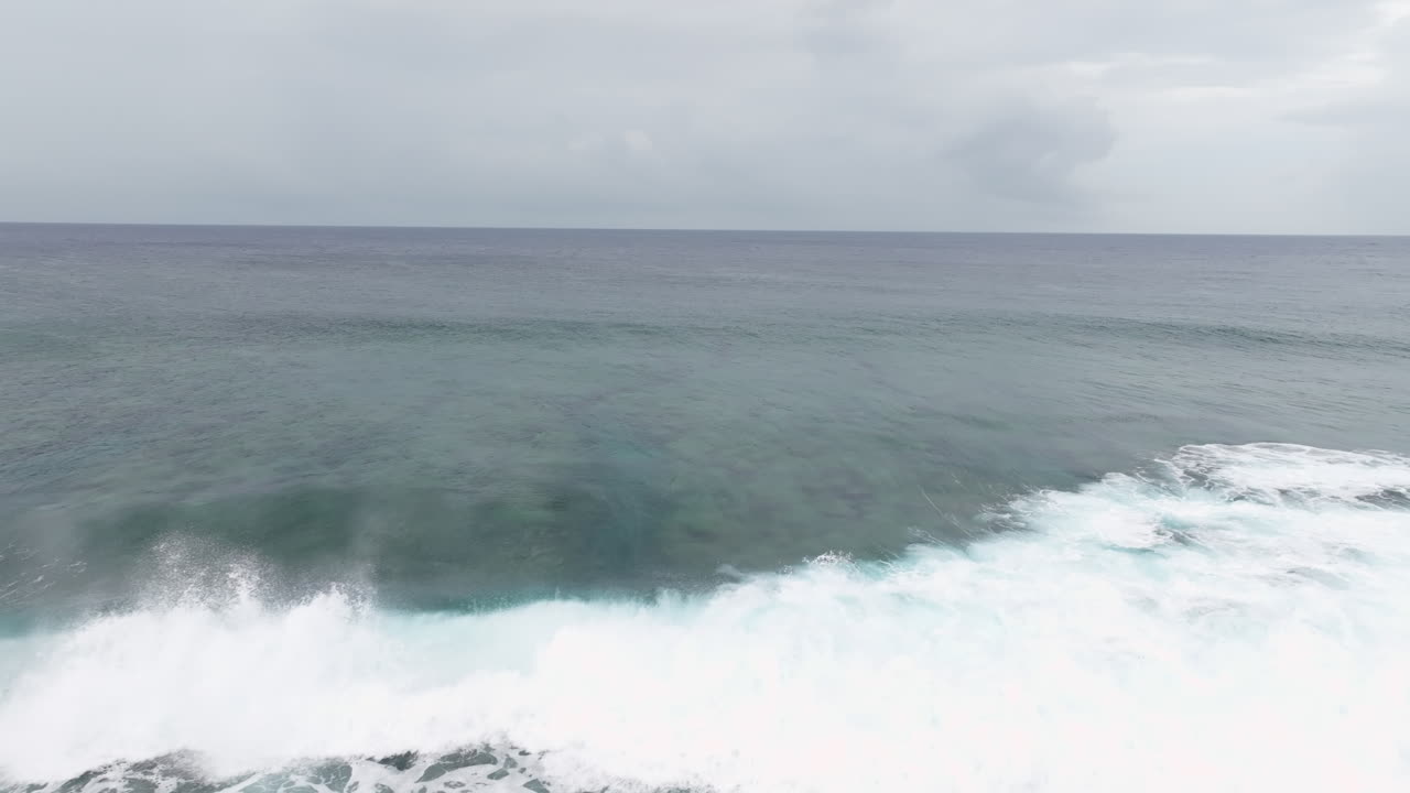 Aerial tracking right slow motion as waves break on shallow fringing reef in ocean water
