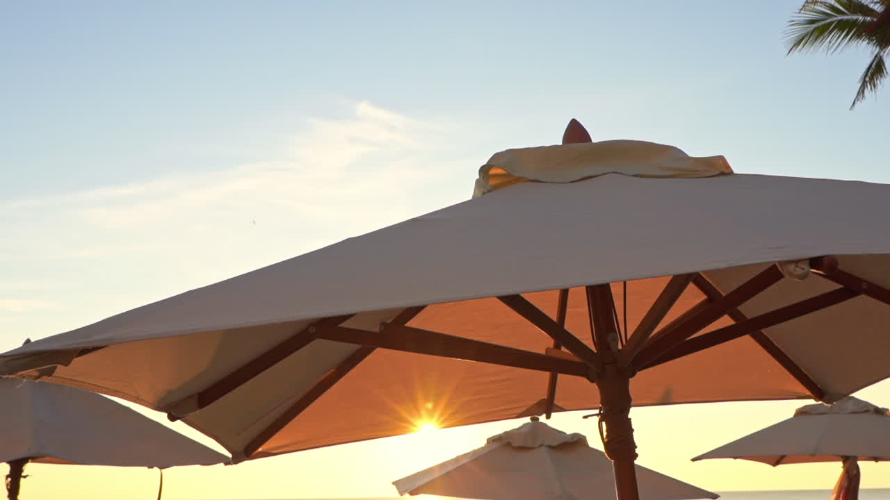 Panning shot of beach umbrellas revealing the sunset in between them