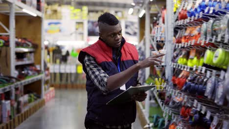 supervisor masculino caminando entre filas en una ferretería examinando productos en los estantes con una tableta