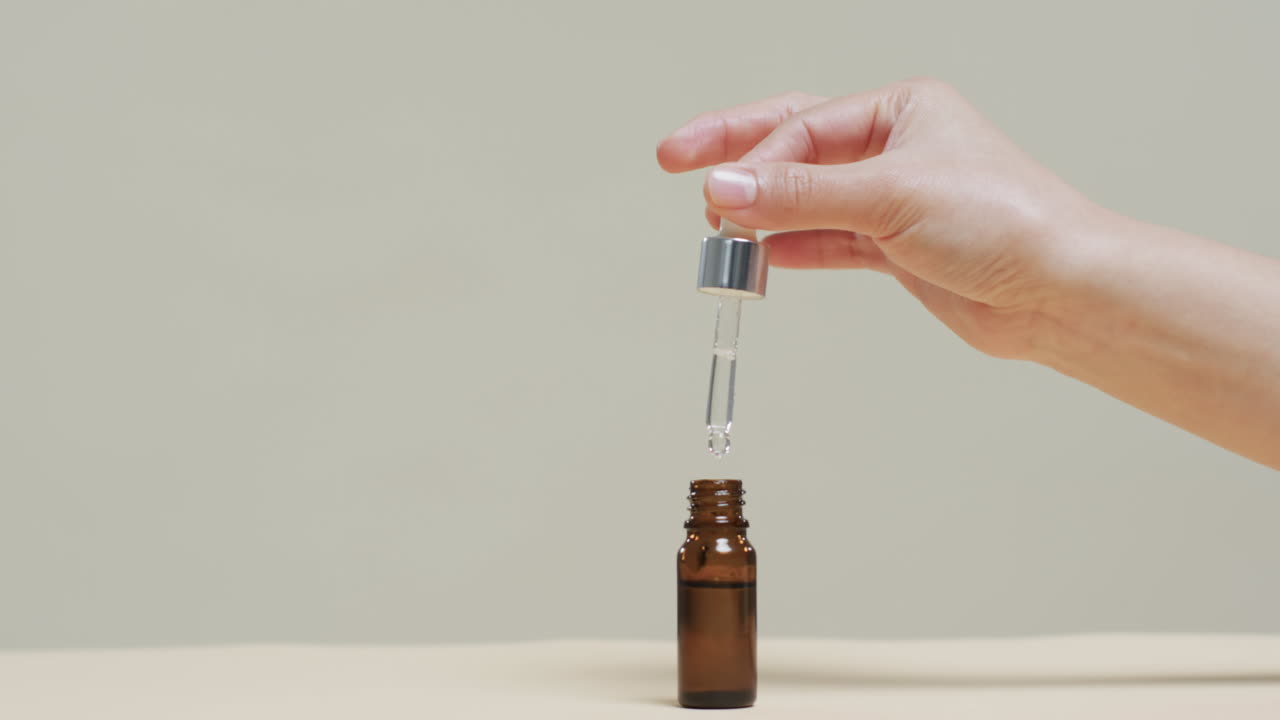 Mano di donna che preleva cosmetico da un flacone su sfondo grigio con spazio per il testo, al rallentatore