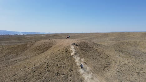 an action-packed, 4k drone shot of two motocross riders hitting a big hill jump, in the desert-like terrain of grand valley ohv area, located in grand junction, colorado