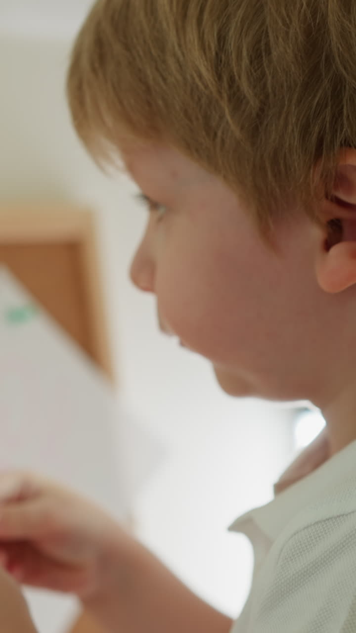 소년은 핀과 그림으로 코크 보드에 종이 한 조각을 부착하려고하지만 손에서 빠져 나갑니다 느린 동작. 유치원 아이는 컬러 종이를 잘라서 으로 근접으로 볼 수 있습니다.