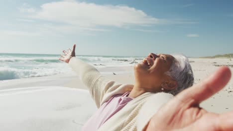 portrait of happy senior hispanic woman standing on beach and raising hands