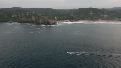 Aerial-tracks-motor-boat-rounding-rocky-headland-by-Mazunte-beach-sand