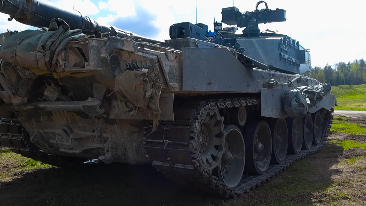 Rare low angle close up footage of a British Challenger 2 4034 army military amored tank standing still and running in a grassy green field during a sunny day. Tanks has a huge weapon cannon for war.