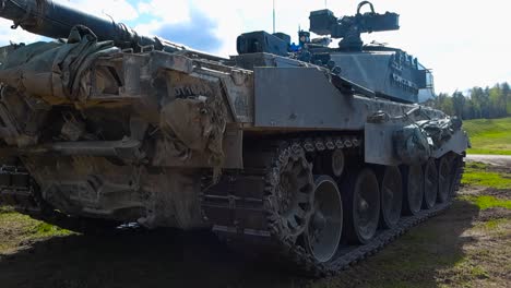 rare low angle close up footage of a british challenger 2 4034 army military amored tank standing still and running in a grassy green field during a sunny day. tanks has a huge weapon cannon for war.