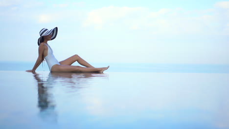 Mujer-Pequeña-En-Traje-De-Baño-Y-Sombrero-De-Verano-Sentada-En-La-Piscina-Infinita-Chocó-Con-El-Horizonte-Del-Mar