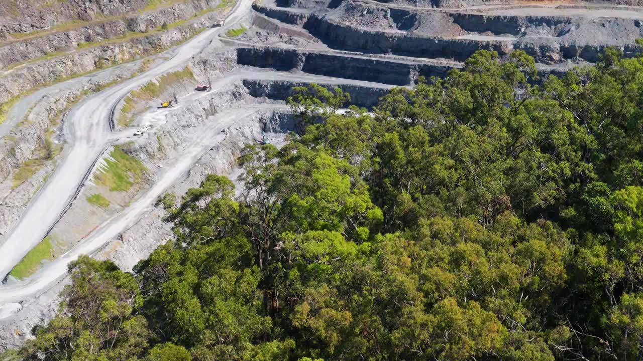 Drone footage captures a terraced quarry surrounded by lush greenery and turquoise water under bright daylight