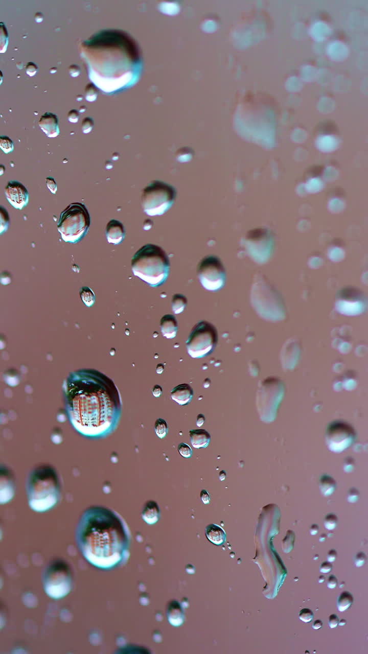 Big raindrops on glass window background. Slow motion of water drops flowing on the glass in a rainy weather. Macro shot. Vertical video