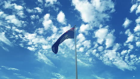 bandera australiana ondeando en el viento con cielo azul y nubes esponjosas en segundo plano