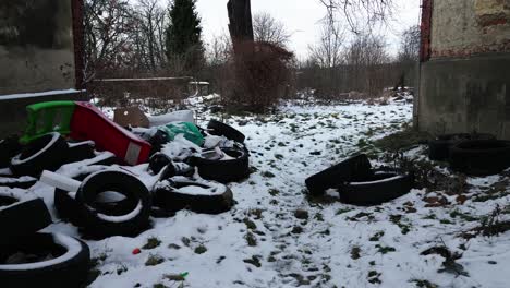 an abandoned, snowy outdoor space between houses littered with discarded tires and trash