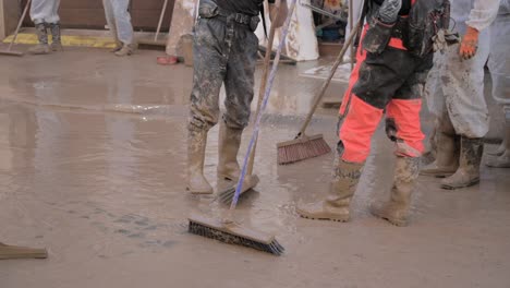 workers wearing boots and protective gear clean up muddy water with large brushes after a flood in valencia