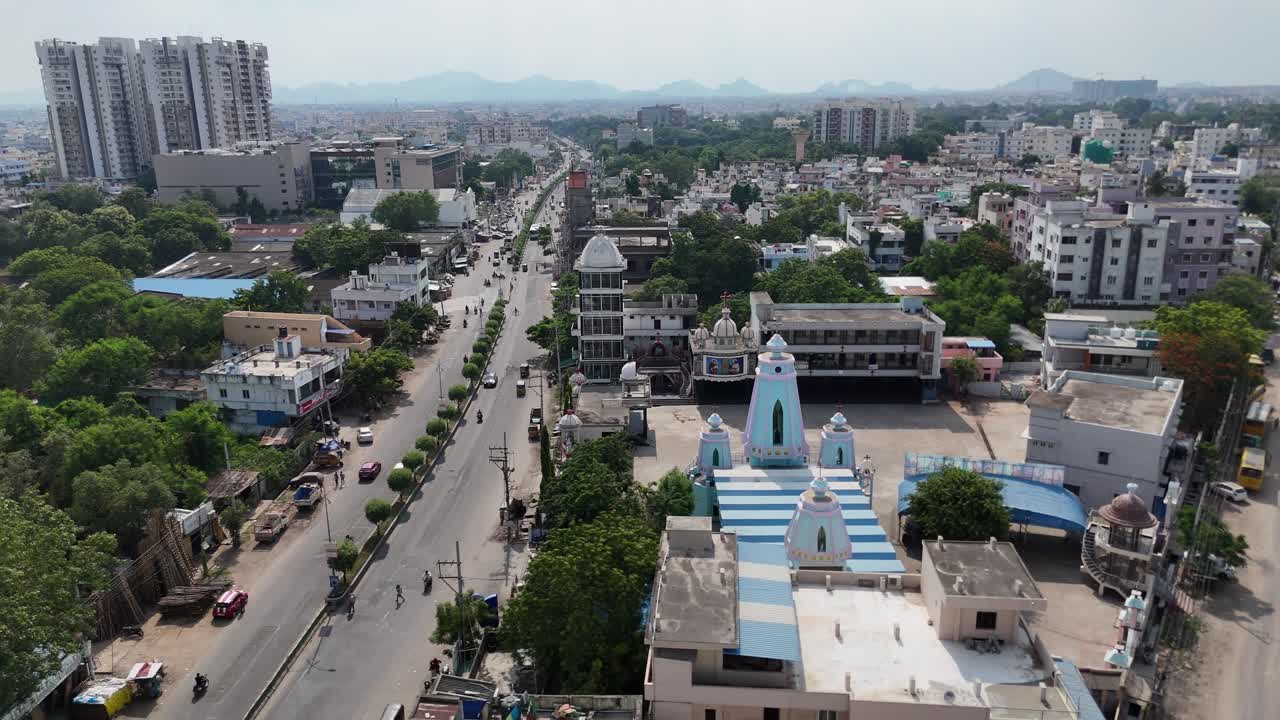 Ripresa aerea della città di Vijayawada con strutture urbane, spazi verdi e una collina panoramica che domina lo sfondo.