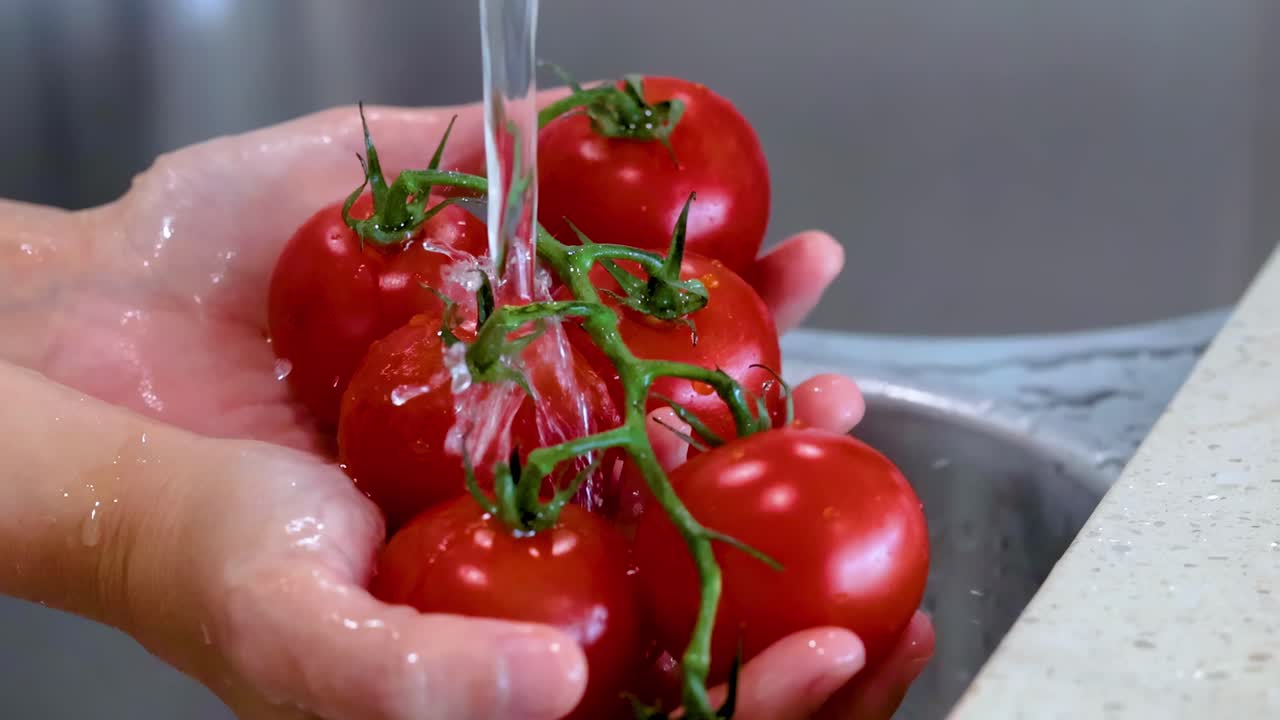 Close-up of hands washing vine tomatoes under a steady stream of water in a kitchen sink.