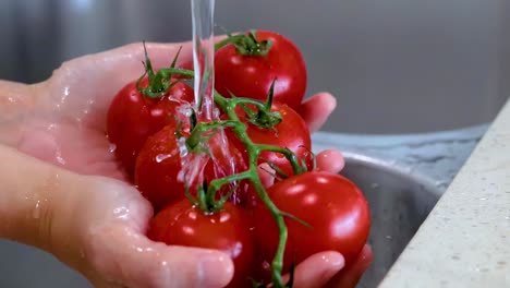 close-up of hands washing vine tomatoes under a steady stream of water in a kitchen sink.