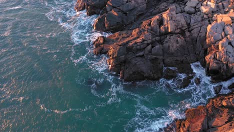 Antena-De-Arriba-Hacia-Abajo-De-Las-Olas-Rompiendo-En-Las-Rocas-Debajo-Del-Faro-Nubble-En-Maine-Iluminado-Por-Un-Frío-Amanecer-De-Diciembre