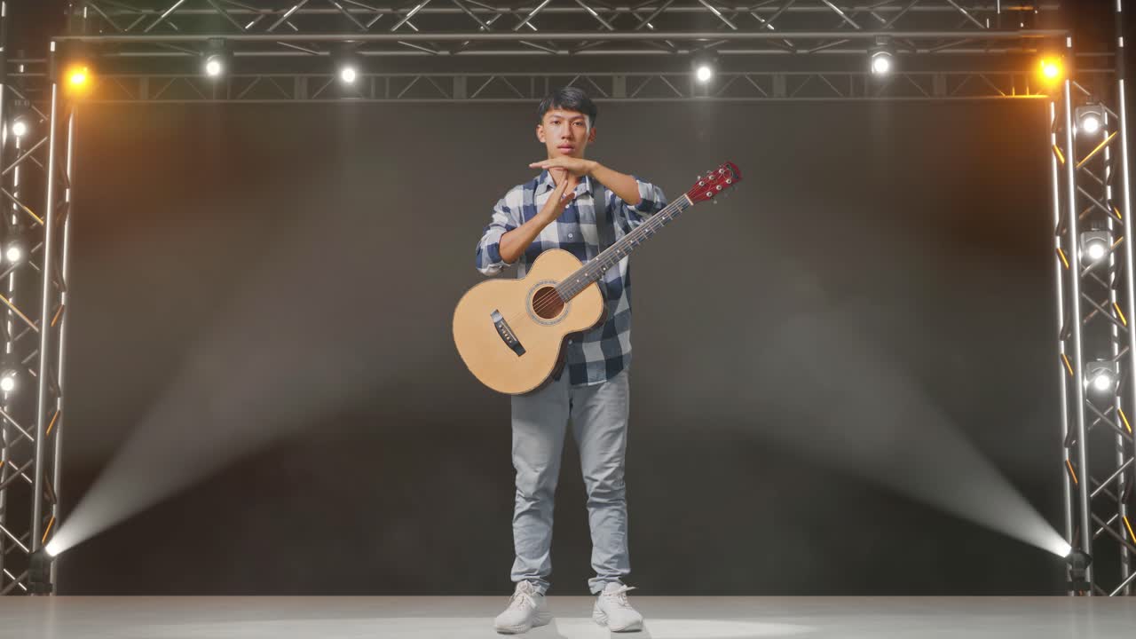 cuerpo lleno de adolescente asiático con guitarra haciendo tiempo fuera gesto con las manos en el escenario