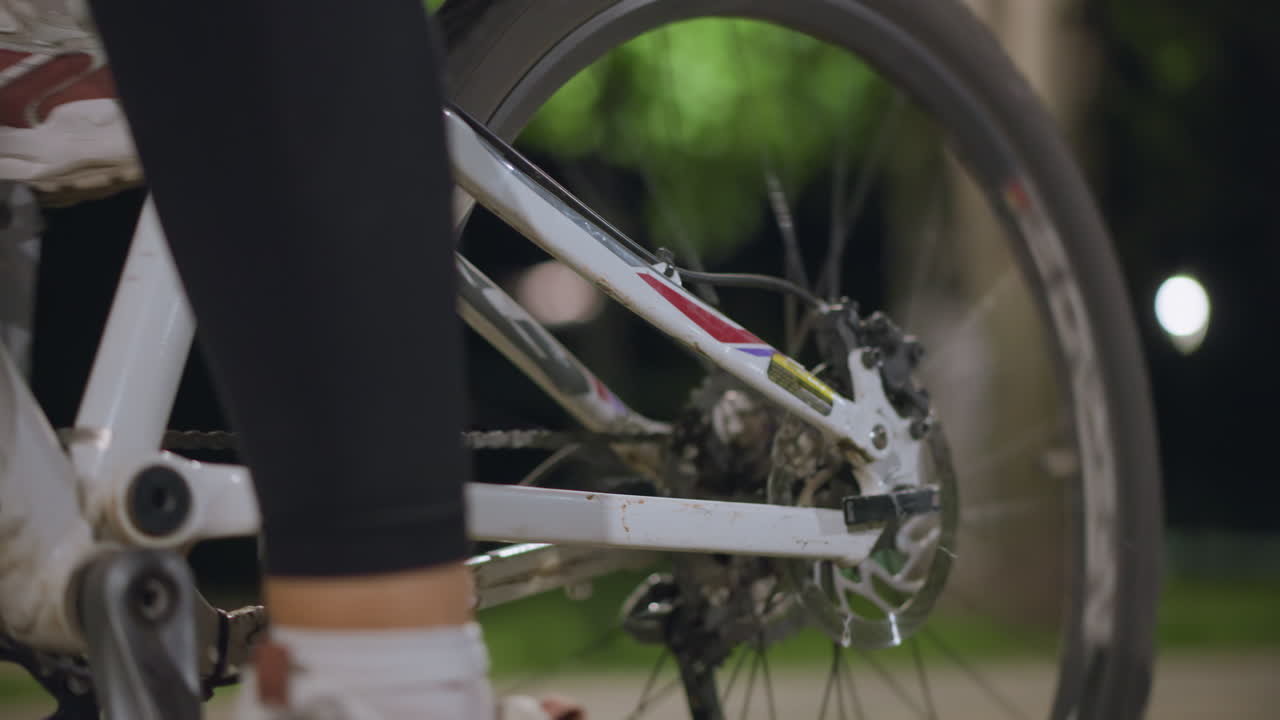 Sneaker Pressing Bicycle Pedal And Crank, Close View Of Foot Motion And Rotating Chain, Energetic Cadence On Park Path Under Soft Lights, Athletic Push And Smooth Drivetrain Action