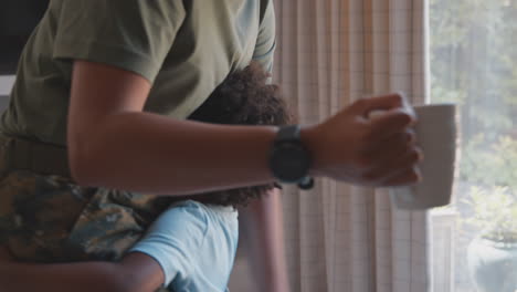 primer plano del hijo abrazando las piernas de la madre del ejército en uniforme en casa de licencia en la cocina de la familia