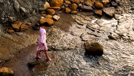 adorable caucasian brunette girl in light pink dress walk by the seashore at sunrise time