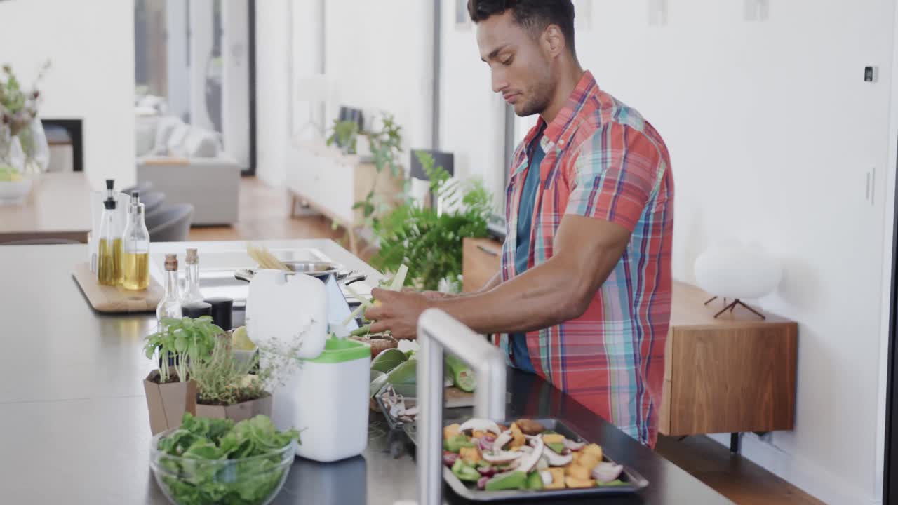 hombre biracial preparando comida, compostaje de residuos vegetales en una cocina moderna, cámara lenta