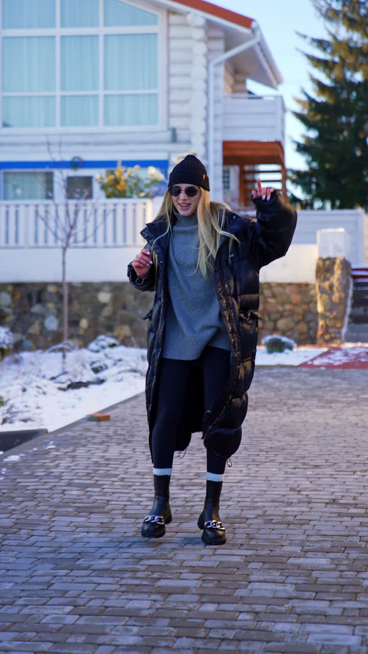 Energetic Caucasian lady in warm clothes and sunglasses dances outdoors. Woman turns around putting off her coat. Vertical video.