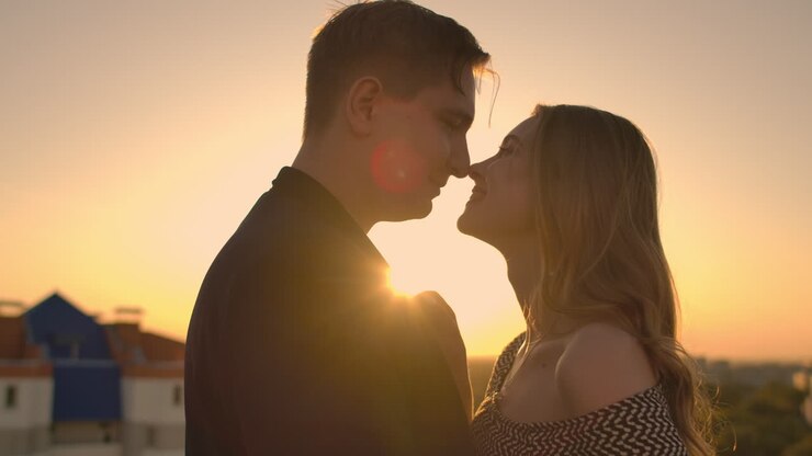 Lovely sweet happines couple sit on the roof top with amazing sunset view on the urban city town. They love each other hugs very tenderness sun goes between hair