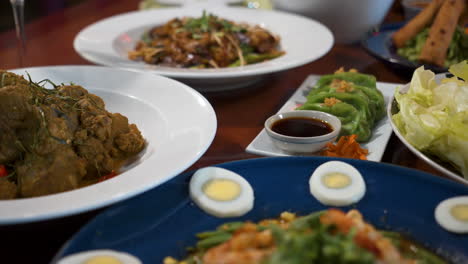 a tabletop filled with asian food, lots of unique thai dishes in crowded onto restaurant table, slider close up 4k