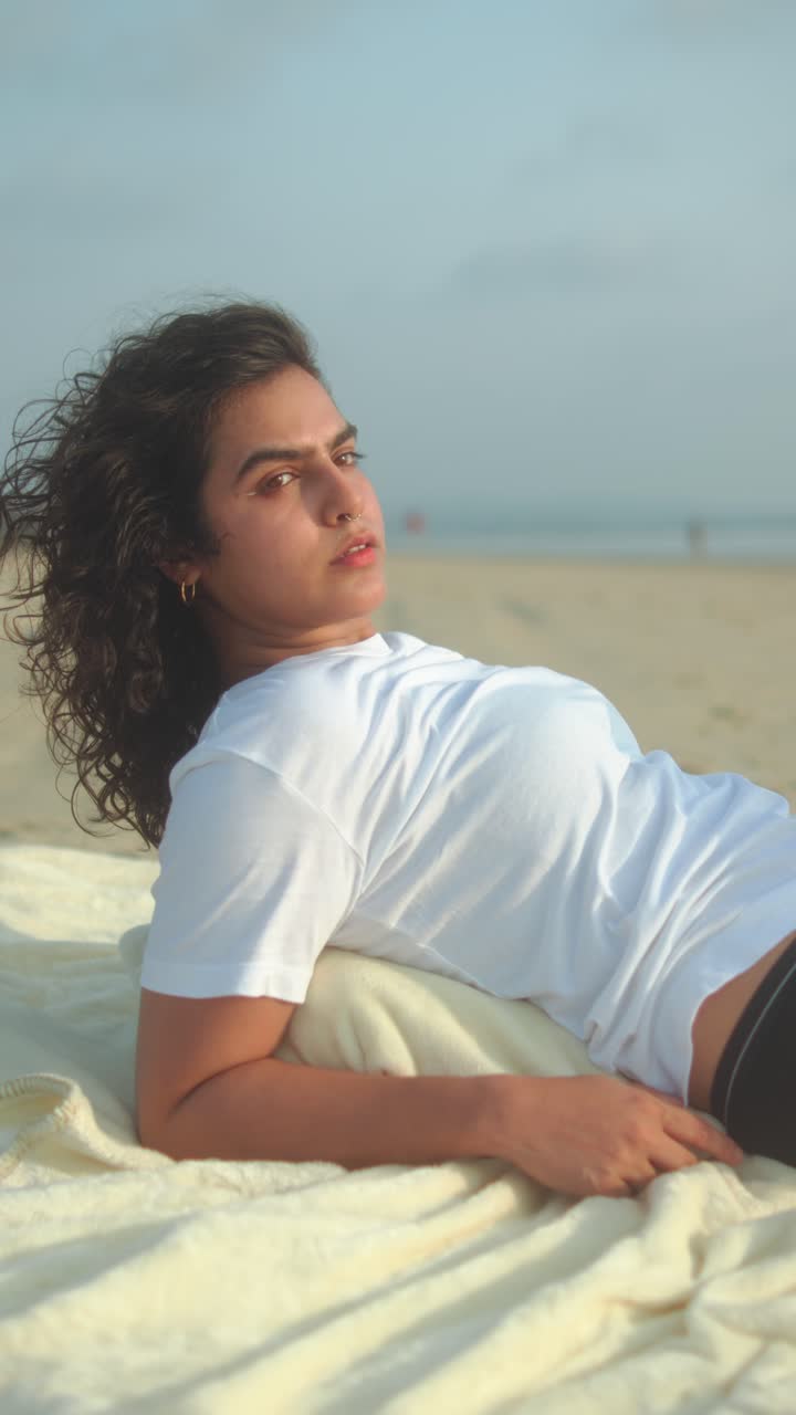Sdraiata sulla spiaggia, donna rilassata che guarda in lontananza, luce dell'ora d'oro