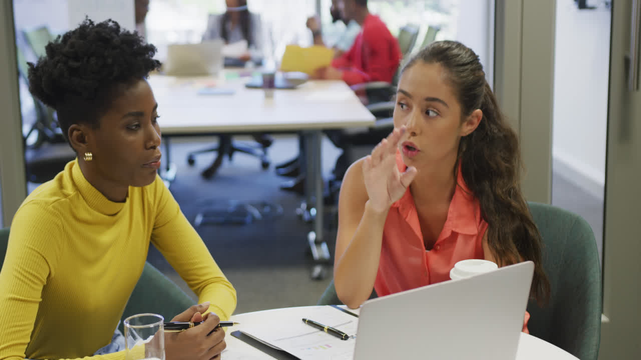 Diverse female business colleagues talking and using laptop in office