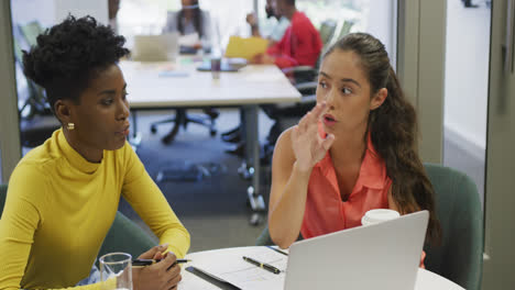 Diverse-female-business-colleagues-talking-and-using-laptop-in-office