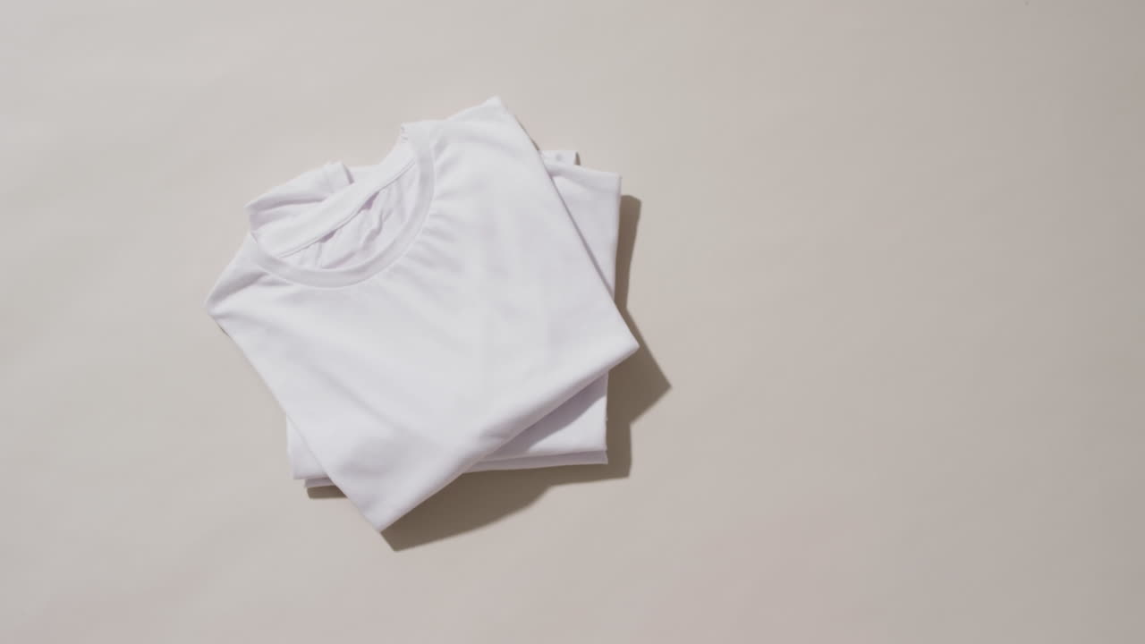 Video of stack of folded white t shirts with copy space on white background