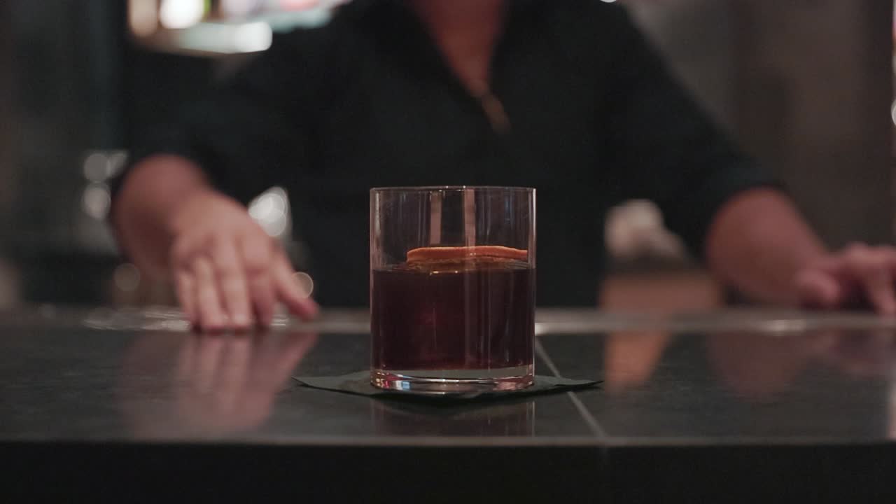 Bartender slides a whiskey cocktail across the bar