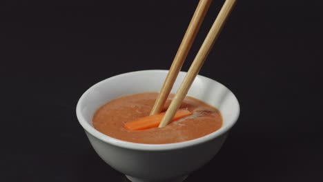 close up of carrot dipping to shabu shabu dip sauce by chopsticks on the black background