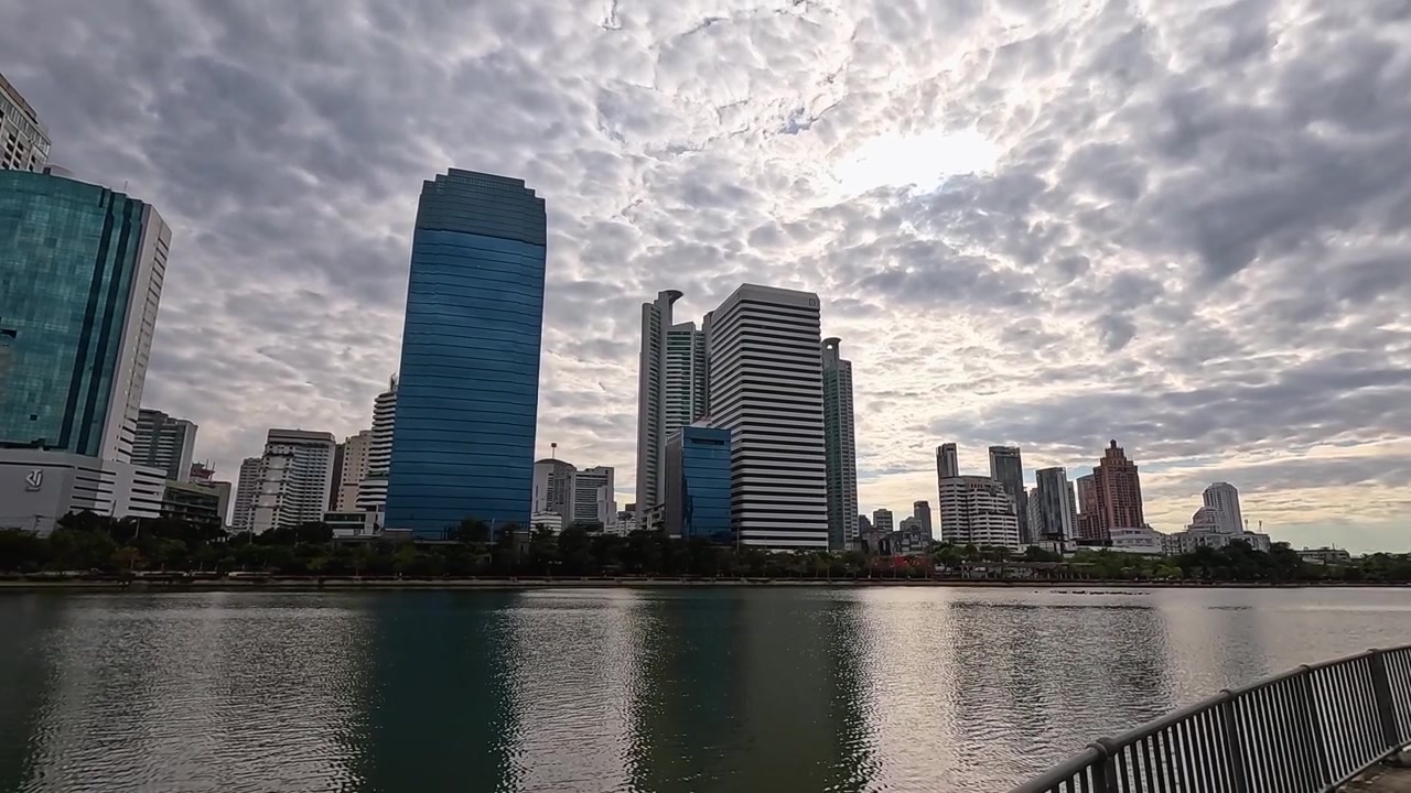 Ampla panorâmica de uma paisagem urbana metropolitana refletindo em um lago calmo sob céus nublados