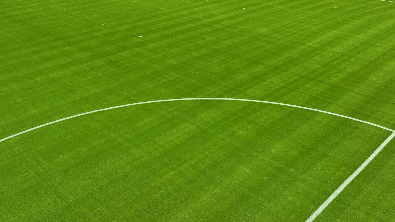 밝은 낮빛 아래에서 색 선이 보이는 활기찬 초록색 축구장의 근접, 낮은 공중 촬영