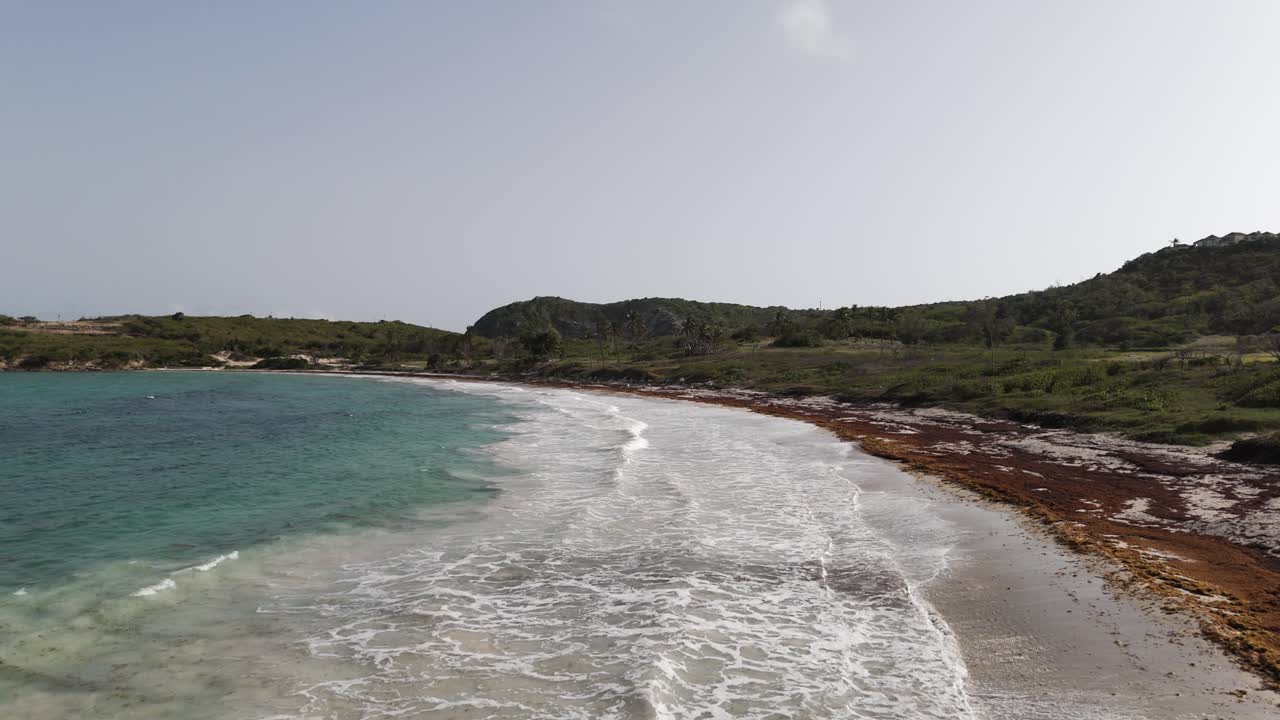 Spiaggia di Half Moon Bay ad Antigua con le onde che si infrangono a riva e rigogliose colline verdi sullo sfondo