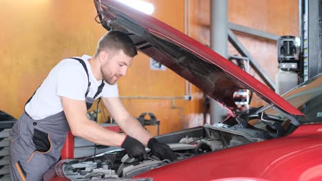 male mechanic working on a red car engine in a garage