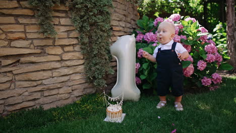 lovely caucasian baby boy stands in the garden near the balloon of number one shape. little kid celebrating first year of life.