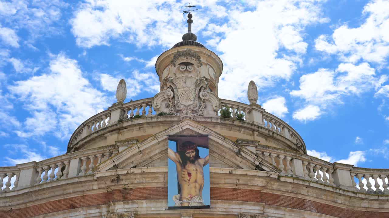 Banner of Jesus Christ on the Royal Church of San Antonio in Aranjuez, Spain. A symbol of faith on a fine example of 18th-century Spanish Baroque architecture under a vast, partly cloudy sky.