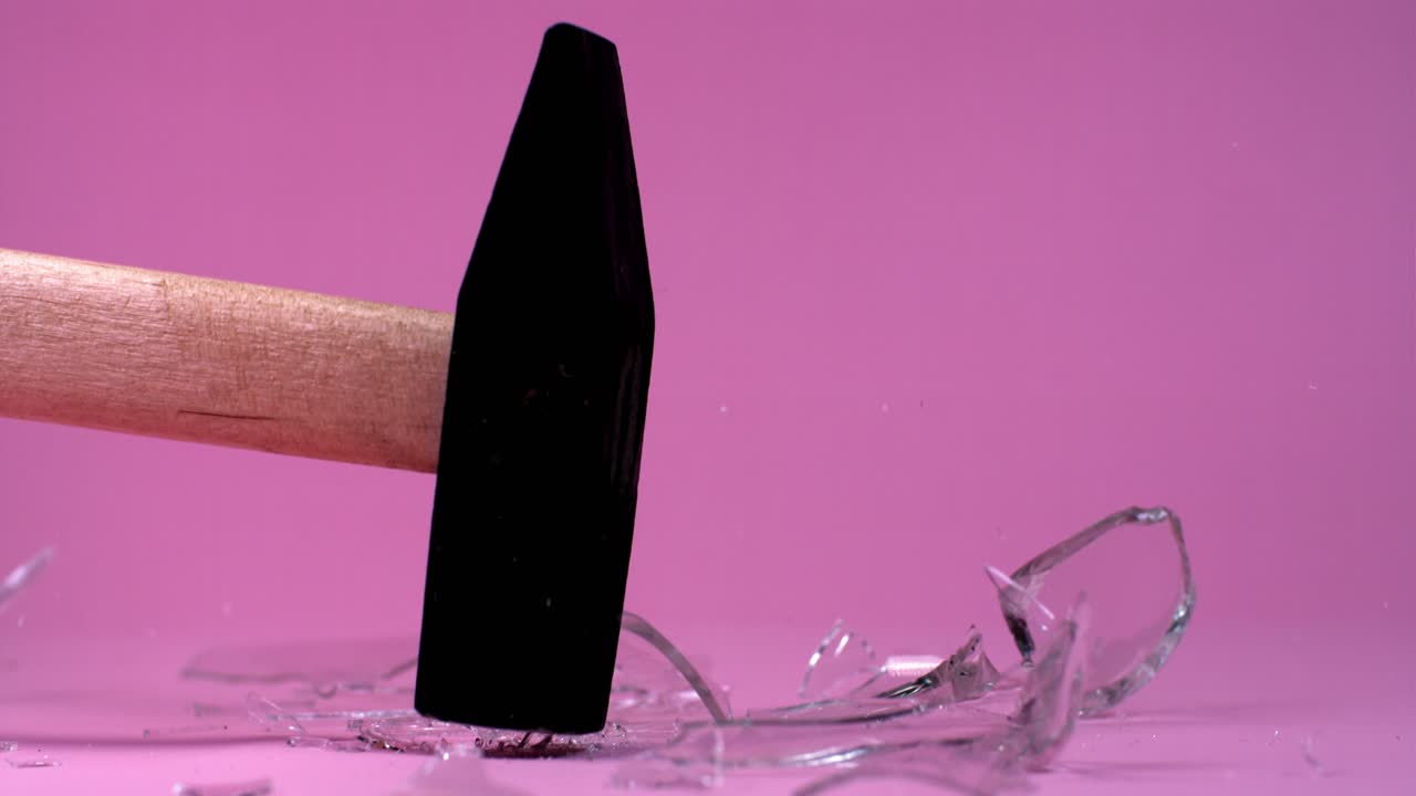 un martillo rompiendo vidrio sobre un fondo rosado