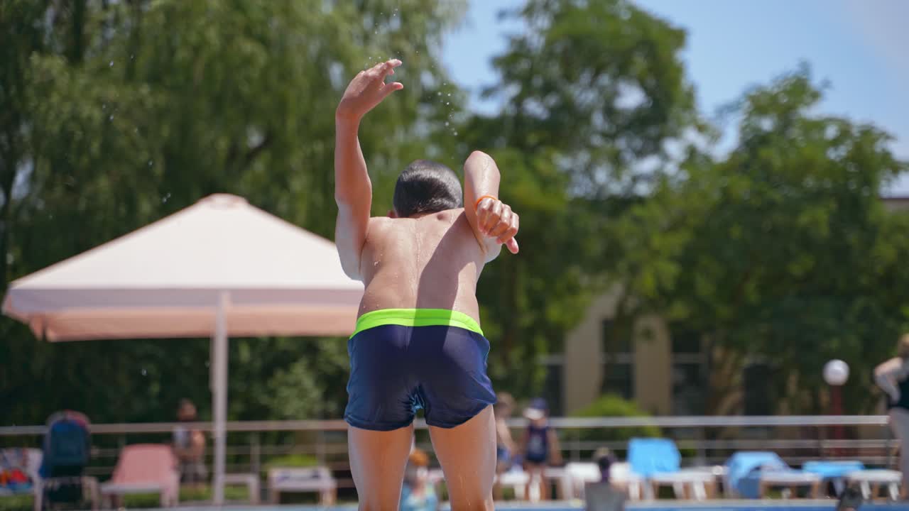 Boy jumping into water. Happy boy enjoying time in the swimming pool in summer daytime. Joyful childhood in the water of the pool.