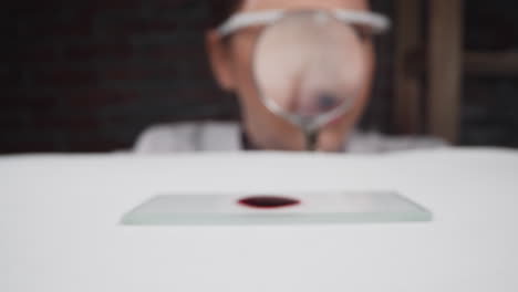 Scientist-looks-through-magnifier-glass-at-blood-sample