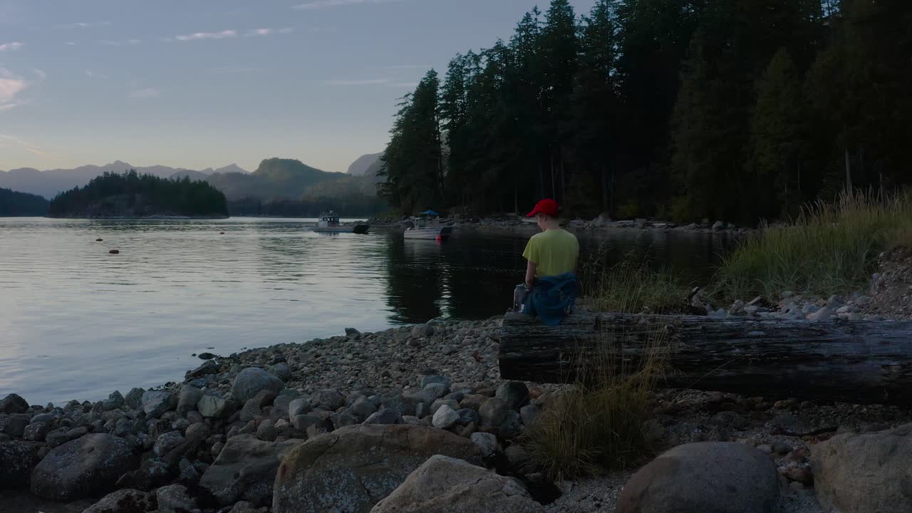 캐나다 브리티시 컬럼비아 에그몬트 근처 선샤인 코스트의 세첼트 입구에서 일몰을 바라보는 나무 통나무에 앉아 있는 사람