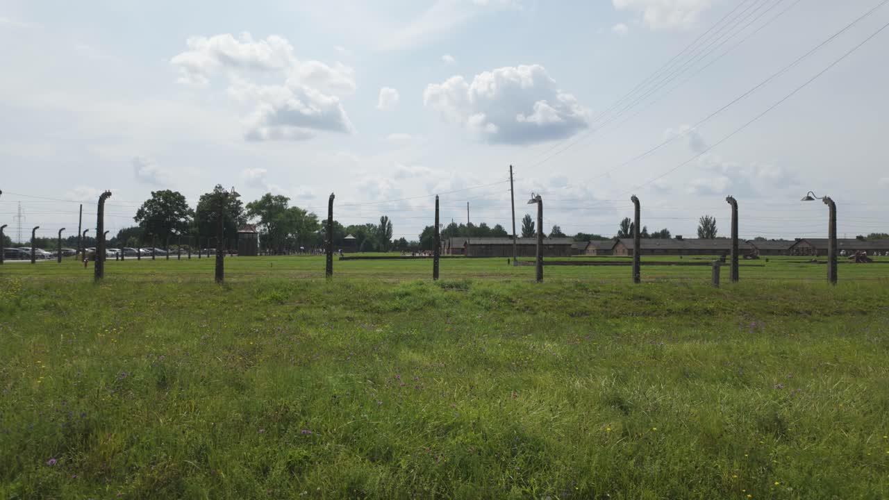 View of Auschwitz Birkenau concentration camp with long wire fence posts amidst a serene landscape. Pan Right Shot