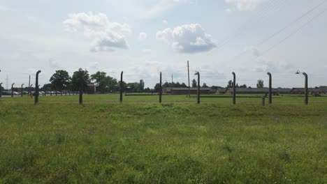 view of auschwitz birkenau concentration camp with long wire fence posts amidst a serene landscape. pan right shot