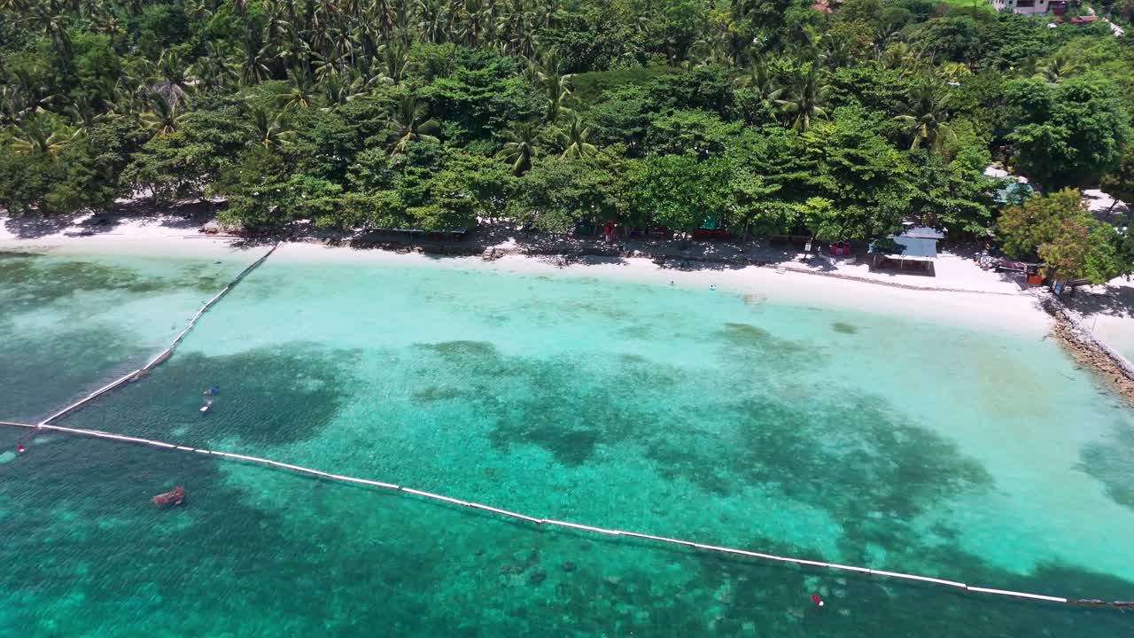 Tropical beach aerial with rock sea walls, clear coral water, and lush tree canopy leading to a remote village—great for travel, lifestyle, or eco-tourism use