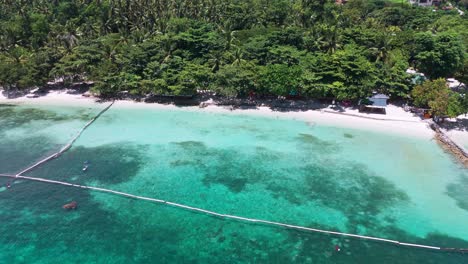 tropical beach aerial with rock sea walls, clear coral water, and lush tree canopy leading to a remote village—great for travel, lifestyle, or eco-tourism use