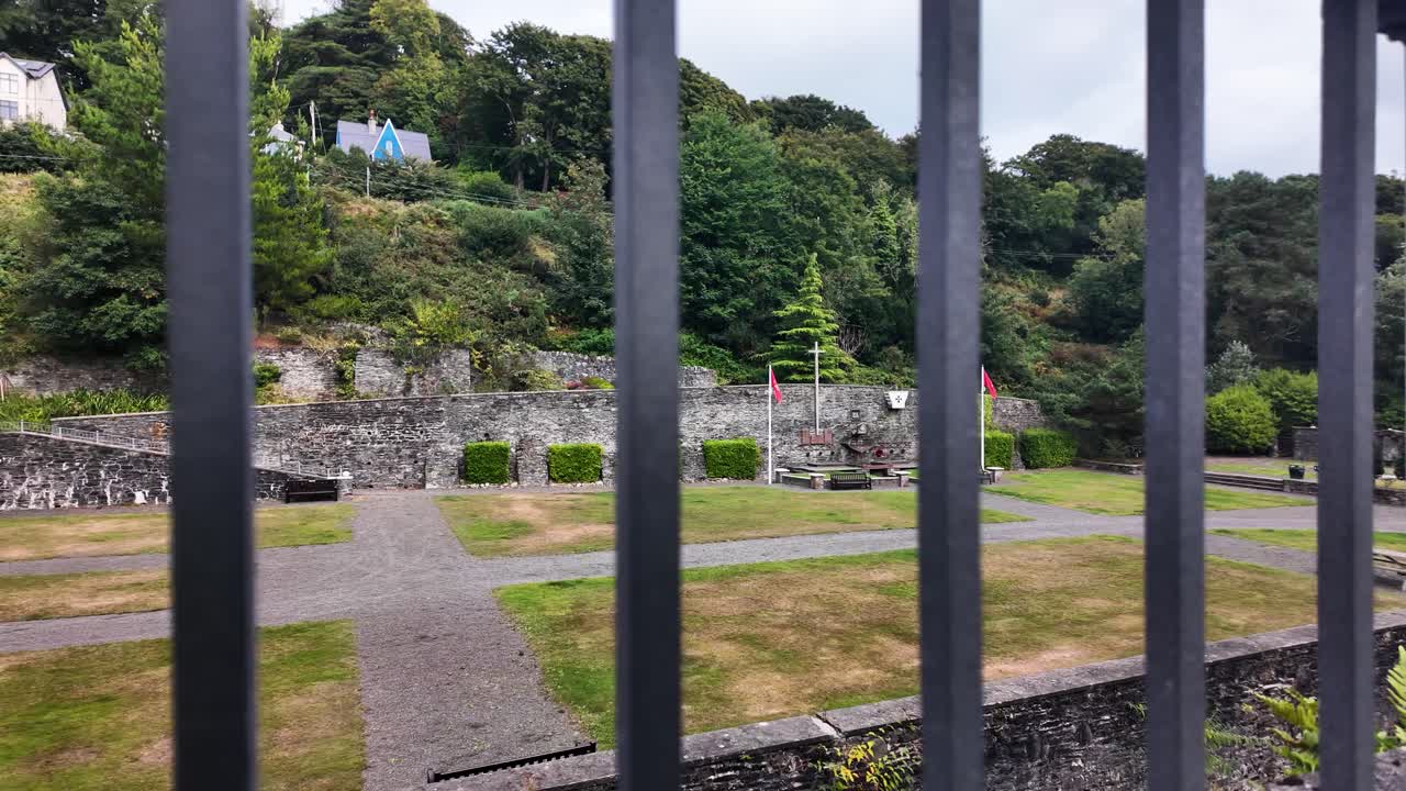 Laxey Glen Gardens park featuring stone walls, green grass, and trees seen through dark iron bars