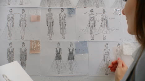 Female-fashion-designer-is-choosing-and-hanging-clothing-sketches-to-wall-for-her-newest-collection.-Light-fabrics.-Female-fashion-designer-is-choosing-and